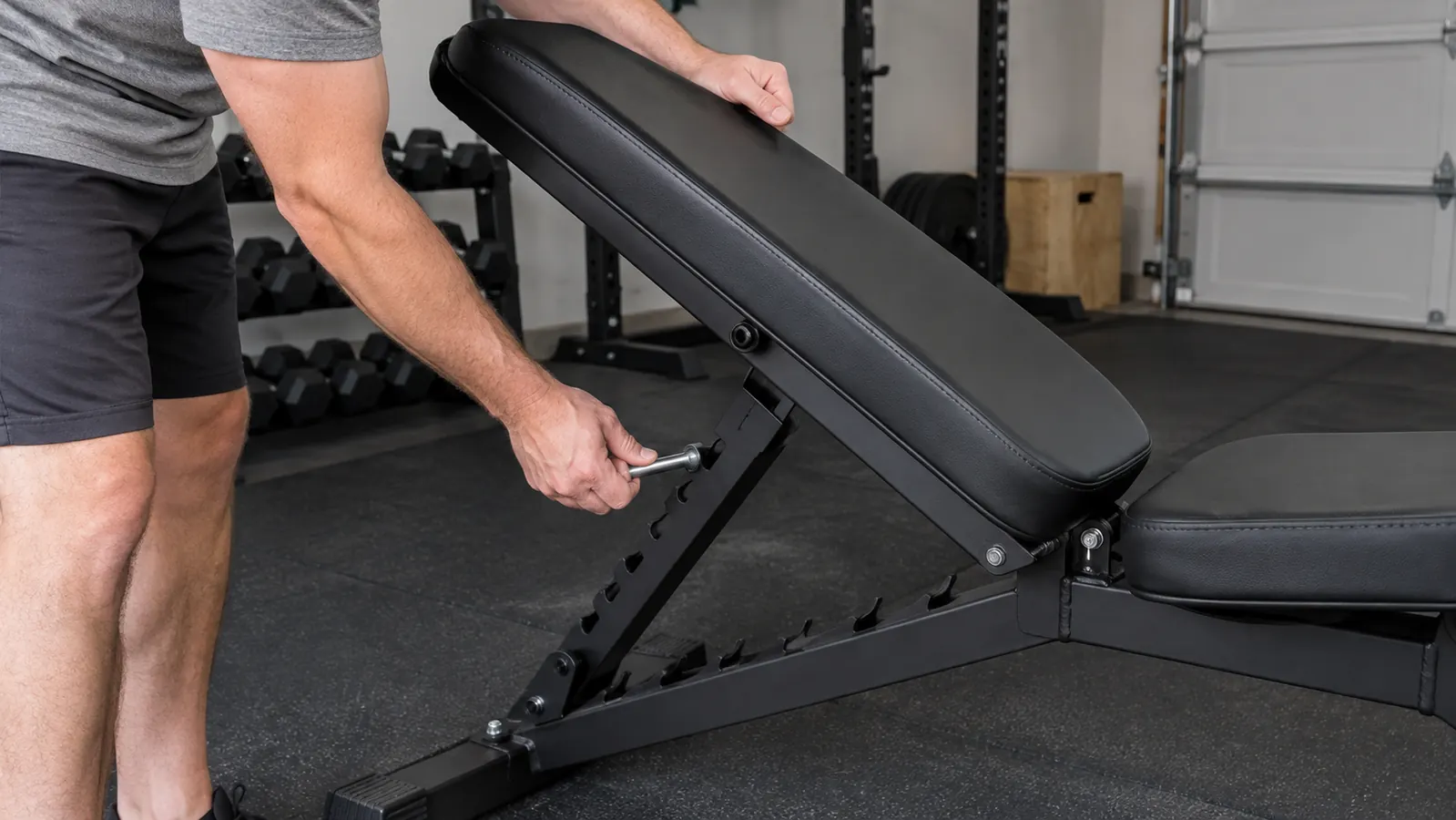 A person's hands adjusting the backrest of an adjustable weight bench in a home garage