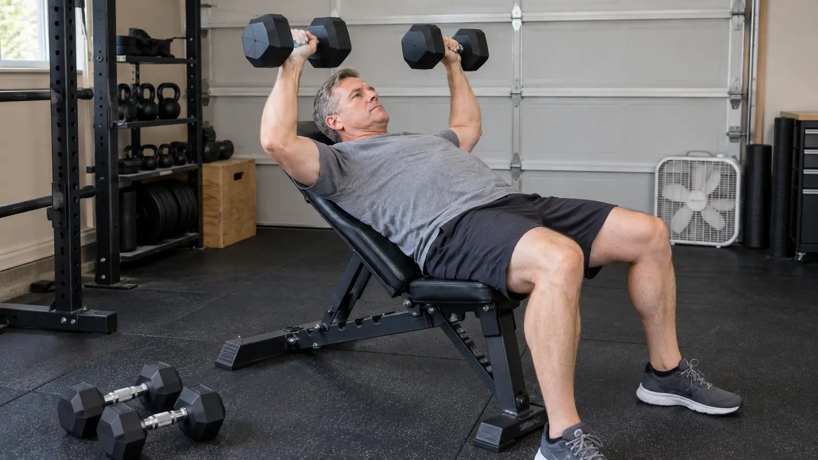 A man in his fifties doing a dumbbell press on an adjustable bench set to a low incline in a garage