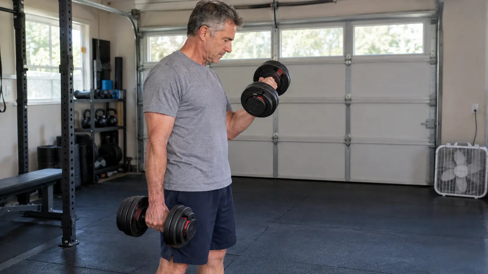 A man in his fifties lifting an adjustable dumbbell in a home garage gym