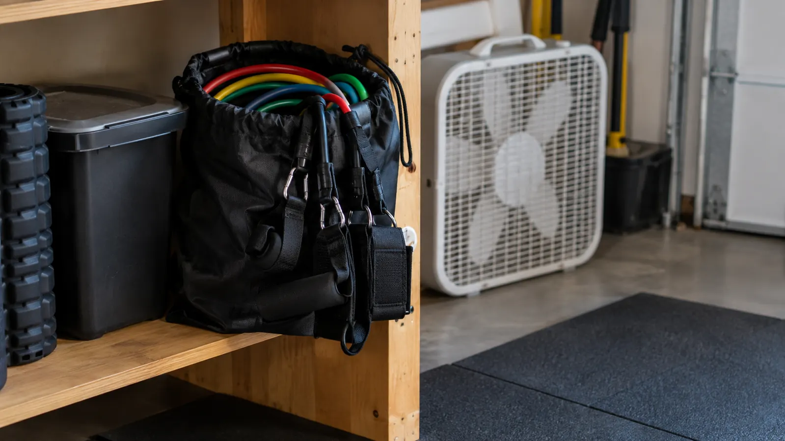 Resistance bands with handles and ankle straps stored in a carry bag on a shelf in a home garage